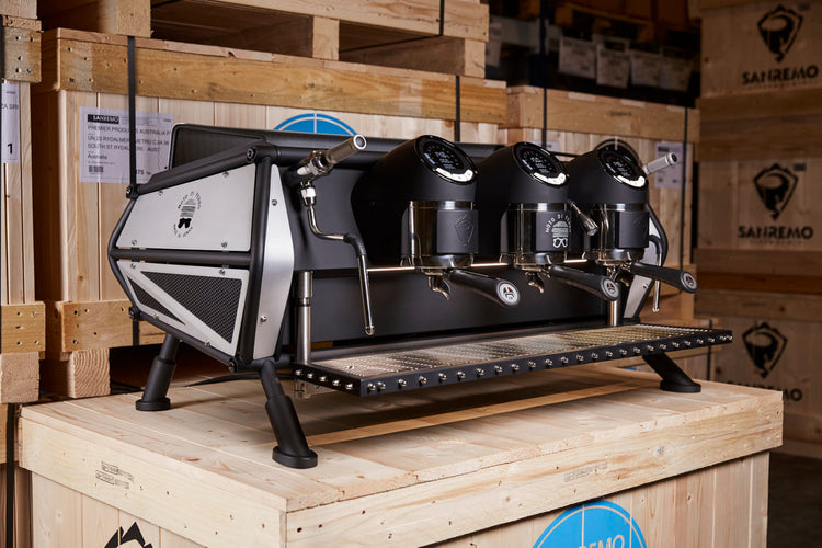 Sanremo Cafe Racer 3-group espresso machine on a wooden crate, with additional crates in the background