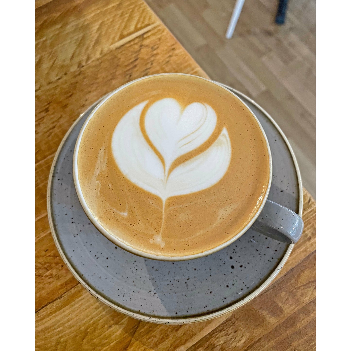 Aerial view of a cup of latte with heart-shaped latte art design on a gray saucer, placed on a wooden table inside lead and vine coffee shop